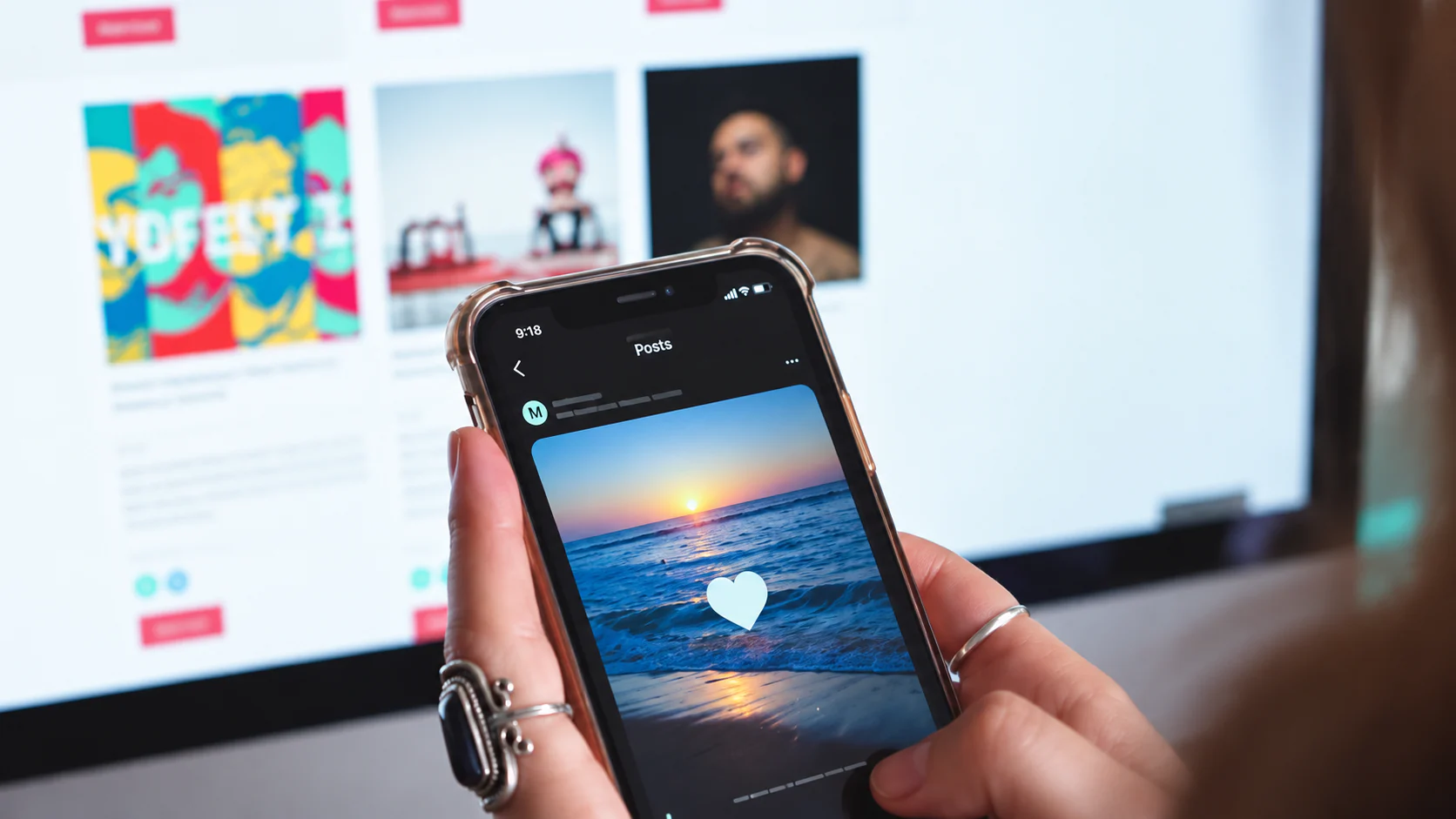 A hand holding a phone with a social media post in front of a computer screen